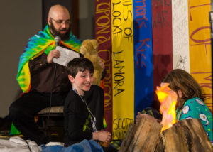 David Abzug and son sitting in front of a campfire on stage at Capricon 36 opening ceremonies