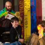 David Abzug and son sitting in front of a campfire on stage at Capricon 36 opening ceremonies